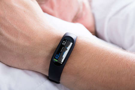 Fitness Activity Tracker With Heartbeat Rate On Man's Hand Over Bedの写真素材