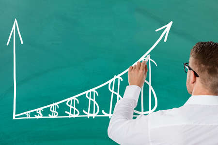 Businessman Showing Inflation Concept With Increasing Dollar Graph On Green Blackboard. Salary Growth Conceptの写真素材