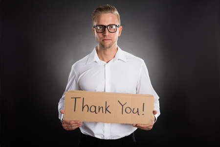 Man Holding Cardboard With Thank You Text Written On It Against Black Backgroundの写真素材