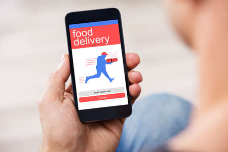 Close-up Of A Man's Hand Holding Smart Phone Showing Food Delivery Application On A Screenの写真素材