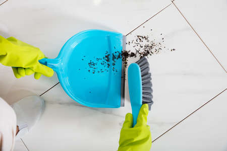 Close-up Of Person Wearing Gloves Sweeping Floor With Broom And Dustpan