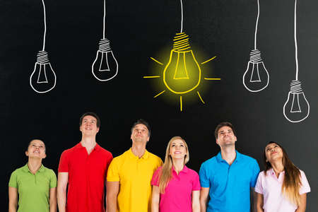 Group Of People Standing In A Row Looking Up At Bright Idea Concept On Blackboardの写真素材