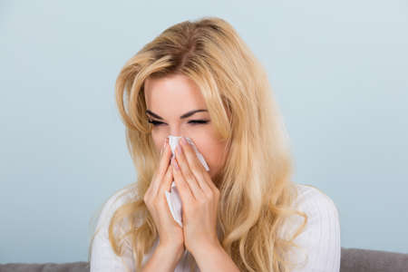 Portrait Of A Woman With Allergy or Flu Sneezing Nose In Tissue Paper On Couchの写真素材