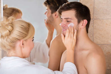 Young Woman Putting Face Cream On Happy Man Nose In Bathroom At Homeの写真素材