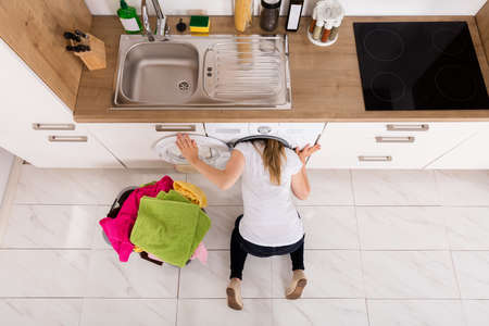 High Angle View Of Young Woman Checking Inside The Washing Machine In Kitchenの写真素材