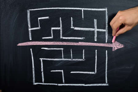 Close-up Of Person Drawing Straight Red Line Over Maze On Blackboardの写真素材