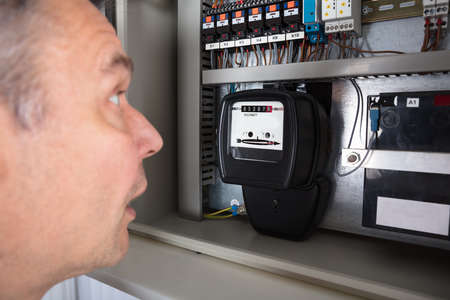 Close-up Of A Shocked Man Looking At Electricity Meter