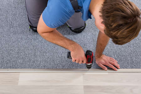 Person's Hand Installing Carpet On Floor Using Wireless Screwdriverの写真素材