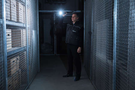 Rear View Of A Security Guard Standing In The Warehouse Holding Flashlightの写真素材