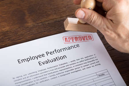High Angle View Of A Person Hand Holding Approved Stamp On Performance Evaluation Formの写真素材