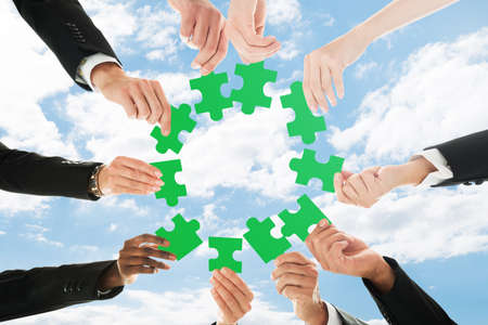 Low Angle View Of A Businesspeople Holding Jigsaw Puzzle Against Sky