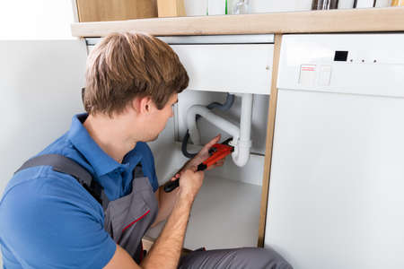 Male Plumber Fixing Sink Pipe With Adjustable Wrench In Kitchen