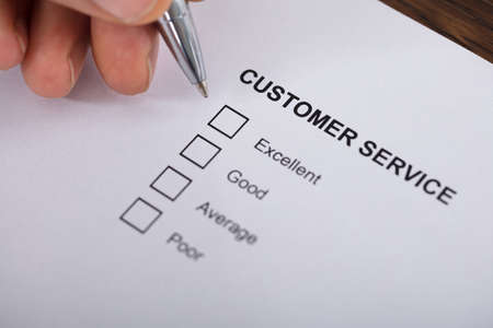 Close-up Of A Person Filling Customer Service Satisfaction Survey Form On Wooden Desk