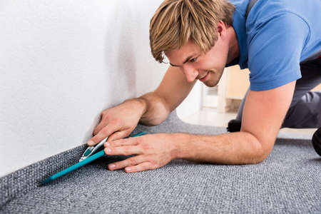 Close-up Of Happy Young Craftsman Cutting Carpet With Cutter At Homeの写真素材
