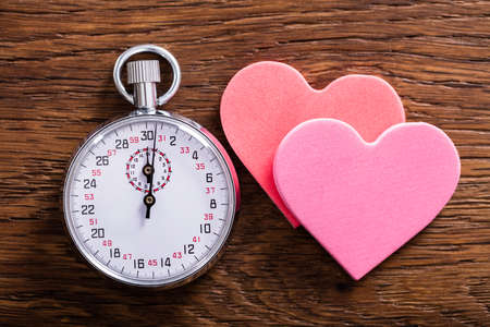 Speed Dating Concept. Two Heart Shapes And A Stop Watch On Wooden Desk