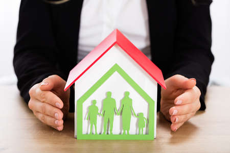 Businesswoman Protecting House Model With Papercut Family House On Wooden Deskの写真素材
