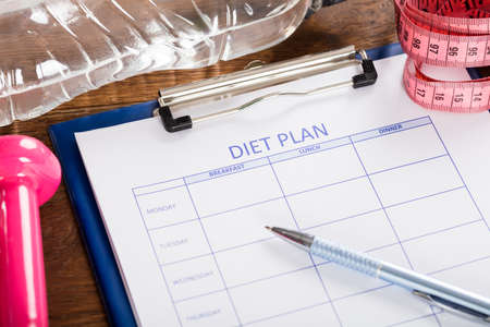 Diet Plan With Dumbbell, Water Bottle And Measuring Tape At Wooden Deskの写真素材