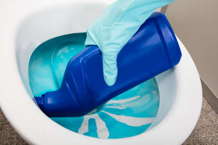 Close-up Of A Person's Hand Wearing Gloves Cleaning Toilet Using Detergent Bottleの写真素材