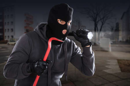 Burglar With A Crowbar And A Flashlight Standing On A Roadsideの写真素材