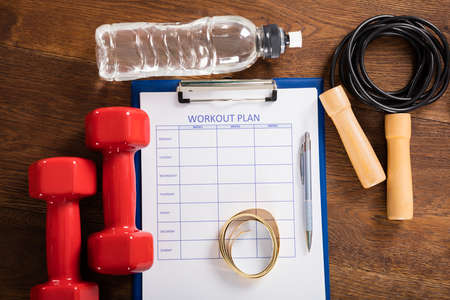 High Angle View Of Workout Plan Form With Fitness Equipments At Deskの写真素材