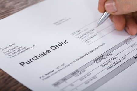 Close-up Of A Person Hand Filling A Purchase Order Form On Wooden Deskの写真素材