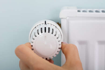 Close-up Of Woman's Hand Adjusting Radiator Thermostat Valve At Homeの写真素材