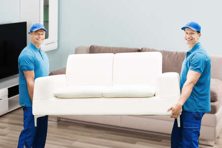 Portrait Of A Two Happy Male Workers Carrying Sofa At Homeの写真素材