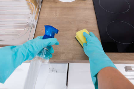 Close-up Of Person Cleaning Kitchen Counter With Sponge And Spray Bottle