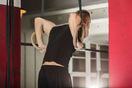 Young Fit Man Pulling Up On Gymnastic Rings In The Gym