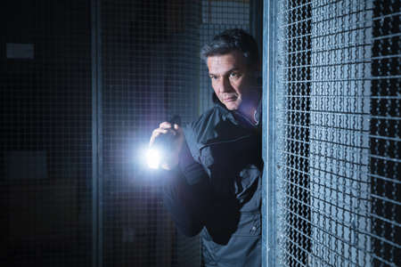 Suspicious Male Security Guard Using Flashlight In The Warehouseの写真素材
