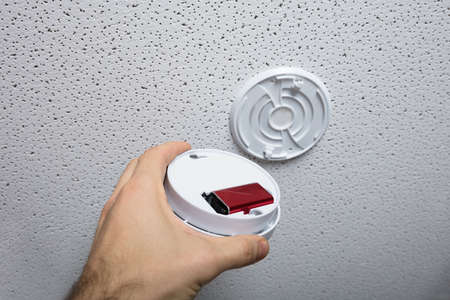 Close-up Of A Person Hand Checking The Battery Of Smoke Detector On Ceiling
