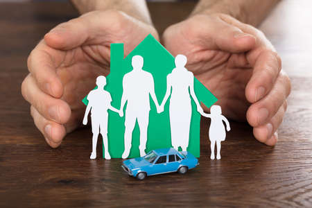 Person Protecting House Model With Family Paper Cut And Car On Wooden Deskの写真素材