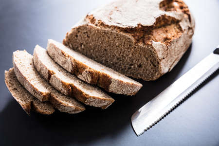 High Angle View Of A Freshly Baked Sliced Bread With Knife On Black Background