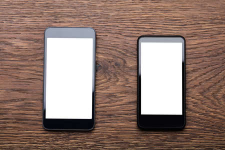 High Angle View Of Two Mobile Phones Showing Blank Screen On Wooden Deskの写真素材