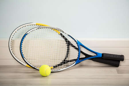 Pair Of Tennis Rackets And A Ball On A Hardwood Floor