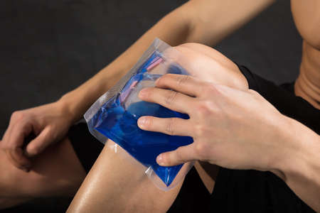 Close-up Of A Person Applying Ice bag On An Injured Knee In The Gymの写真素材