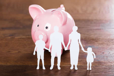 Family Saving Concept With Piggybank And Family Paper Cut On Wooden Desk
