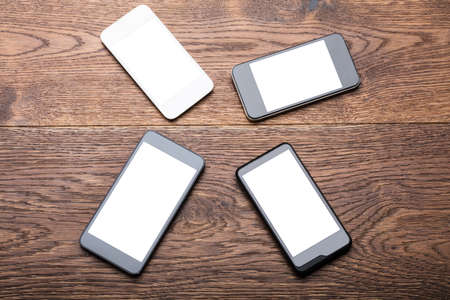High Angle View Of A Group Of Mobile Phones Showing Blank Screen On Wooden Deskの写真素材
