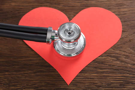 Close-up Of A Red Heart With Stethoscope On Wooden Deskの写真素材