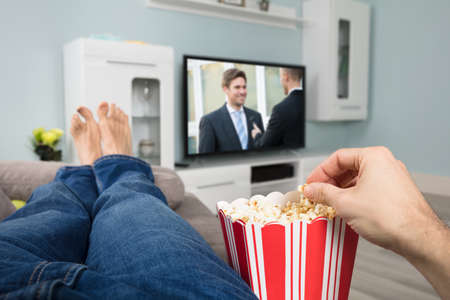 Close-up Of A Person Enjoy Watching Movie On Television While Eating Popcorn