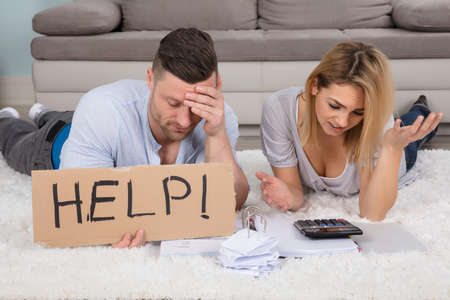 Frustrated Couple Holding Help Sign While Calculating The Bills At Home