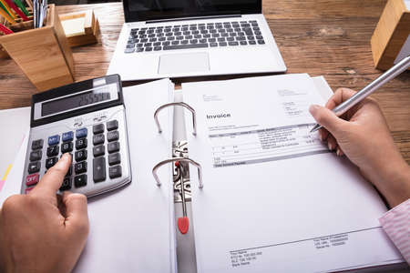 Businesswoman Holding Calculator In Her Hand Calculating Invoice On Deskの写真素材