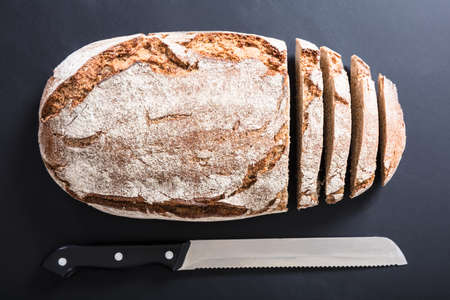 High Angle View Of A Freshly Baked Sliced Bread With Knife On Black Background