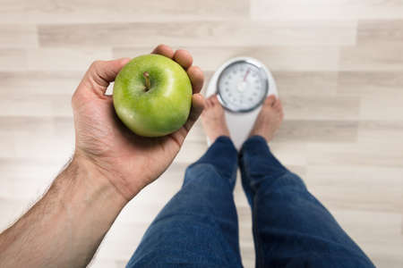 High Angle View Of A Person Measuring Weight While Holding Apple On Weighing Machine