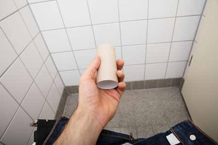Close-up Of A Man's Hand Holding Empty Toilet Paper Roll In Bathroom