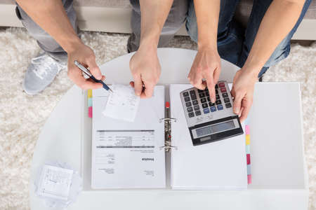 Overhead View Of A Couple Sitting On Couch Calculating Bills