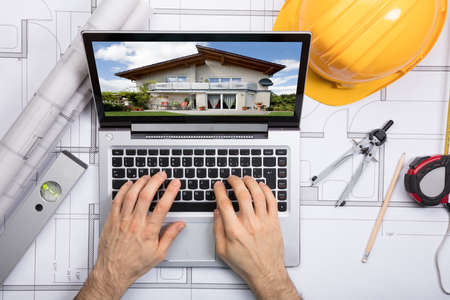 Close-up Of A Architect Using Laptop With A House On Screen Over The Blueprintの写真素材