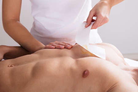 Close-up Of A Woman Waxing Man's Chest With Wax Stripの写真素材