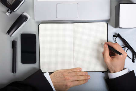 Close-up Of A Person Writing On Checkered Notebook Over The Office Deskの写真素材