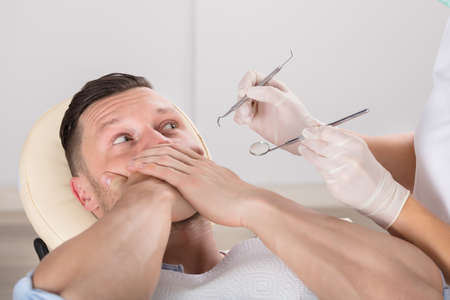 Man Covering His Mouth With Hands While Having Dental Checkup In Clinicの写真素材